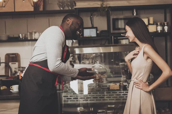 Male barista helps a girl to choose a dessert