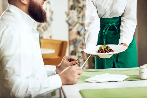 Cameriere ragazza serve il suo piatto in ristorante per un uomo — Foto Stock