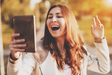 Gülümseyen kız güneşli park sokakta tablet kullanma.