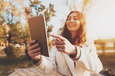 Gülümseyen kız güneşli park sokakta tablet kullanma.