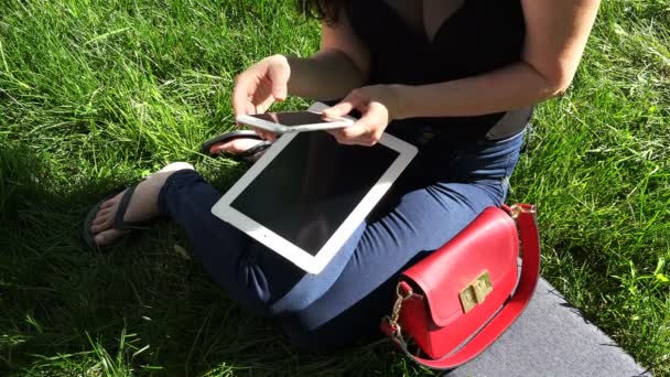 Dziewczyna pracuje z tabletu i telefonu komórkowego w parku — Wideo stockowe