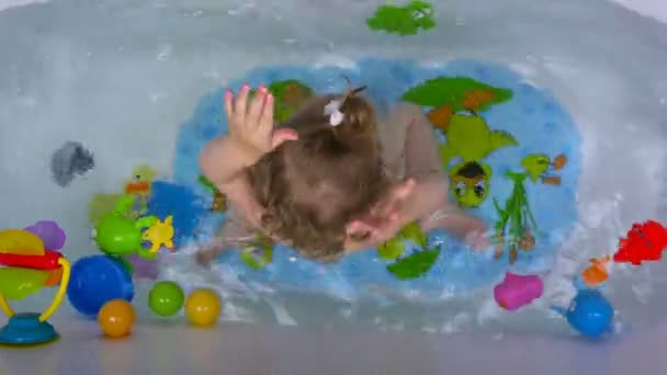 Una niña de dos años en el baño salpicando con agua. Vista desde arriba — Vídeo de stock