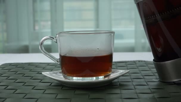 In een transparante beker met thee, aangevuld met theebladeren — Stockvideo