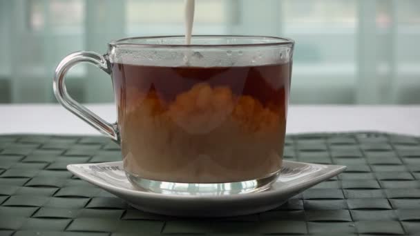 Leche se añade a una taza de vidrio con té — Vídeos de Stock