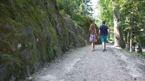 Egy fiatal pár sétál a sziklák mentén a nyári napsütésben — Stock videók