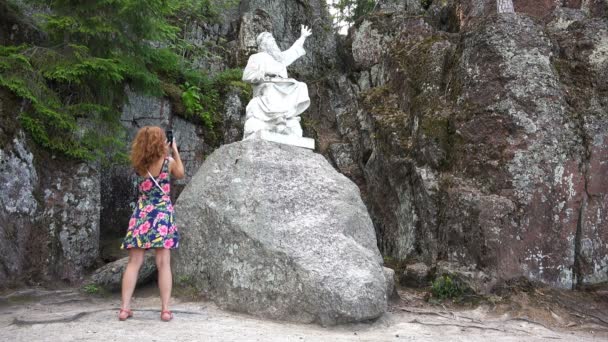 En flicka fotografier på telefonen ett monument på en sten — Stockvideo