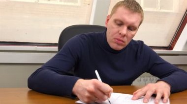 A specialist signs documents and clutches his hands with his head bent over the table