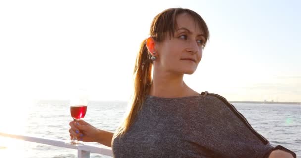 Una joven con una copa de vino tinto está en la cubierta del barco — Vídeos de Stock