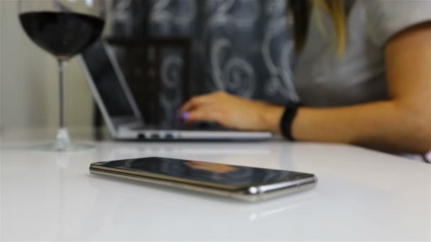 Uma menina trabalha em um laptop e ao lado dela é um smartphone — Vídeo de Stock