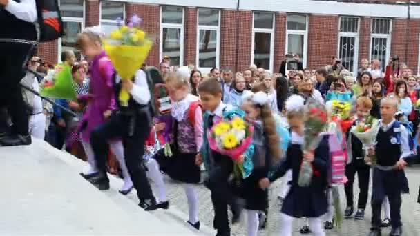Første klasses elever går parvis ind i skolen med blomster – Stock-video