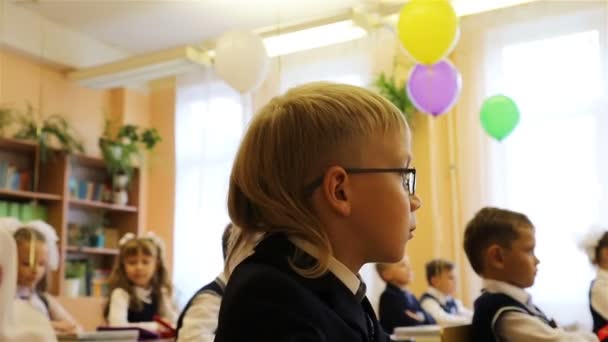 O aluno do primeiro ano de óculos está na aula em sua mesa na escola. — Vídeo de Stock