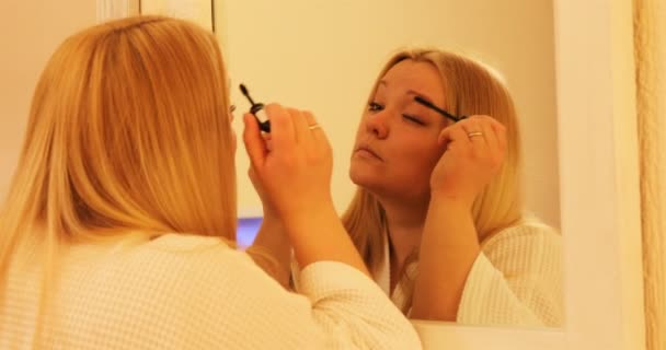 Das Mädchen zieht vor dem großen Spiegel Wimperntusche auf — Stockvideo