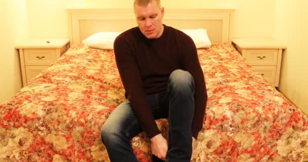 Мужчина сидит на кровати и надевает черные носки — стоковое видео
