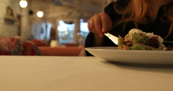 La chica está comiendo la ensalada de verduras usando el tenedor y el cuchillo en la cafetería — Vídeos de Stock