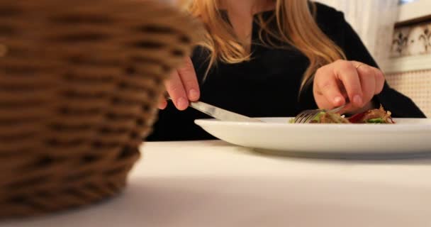 La chica en la mesa blanca está comiendo la ensalada usando el tenedor y el cuchillo. — Vídeo de stock