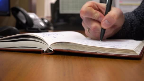 Με ένα μαύρο στυλό, ένας νεαρός άντρας γράφει στο σημειωματάριό του. — Αρχείο Βίντεο