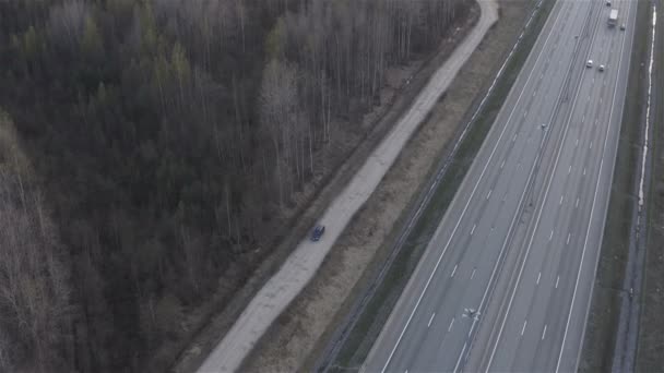 En bil rör sig längs en grusväg längs en motorväg — Stockvideo