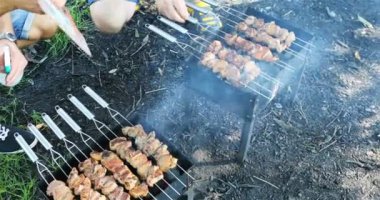 İki ızgarada ızgara kebap yapan adam eti ters çevirip ateşini suyla söndürür.