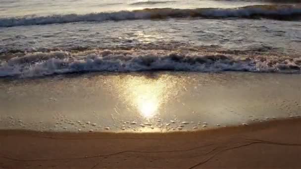 Los rayos del sol se reflejan en el agua de mar que sale con las ondas en la orilla arenosa — Vídeos de Stock