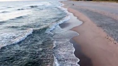 Turistler kumlu bir plajda deniz kıyısında dinleniyor.