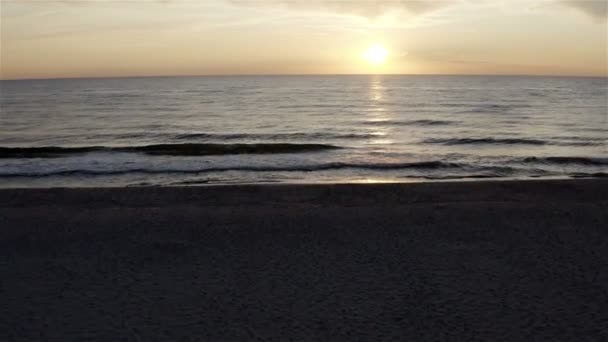 Pe un mal de nisip un val de mare se grăbește împotriva apusului de soare — Videoclip de stoc