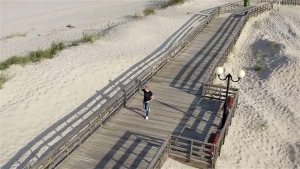 Ein unbemanntes Fahrzeug fliegt um einen Mann herum, der die Promenade entlangläuft — Stockvideo