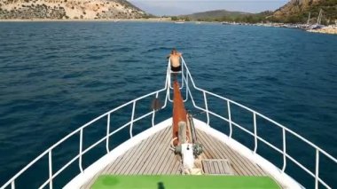 Genç çocuk yatın önünde oturan limana bakıyor.