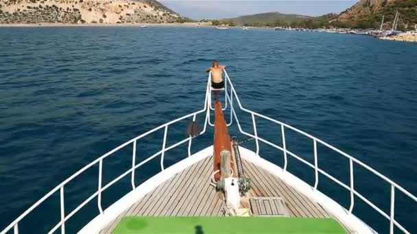 Teenie boy looks at the hafen sitting on the front of the yacht — Stockvideo