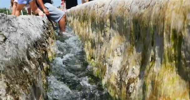 Una corriente de agua de montaña fluye a través de la cuneta, los turistas calientan sus pies — Vídeos de Stock