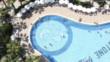 Otelin bölgesinde turistler havuzda yüzer ve güneşlenirler.