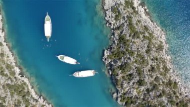 Taş adalar arasında demirlemiş turistli üç beyaz yat.