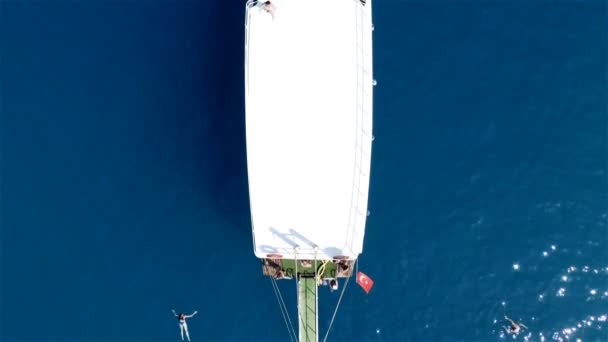 Белая длинная яхта с туристами на борту стоит в голубой лагуне. Аэрофотосъемка — стоковое видео