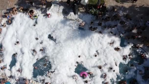 Flocos brancos de espuma ensaboada espalham-se pela piscina com turistas. Uma festa de espuma — Vídeo de Stock