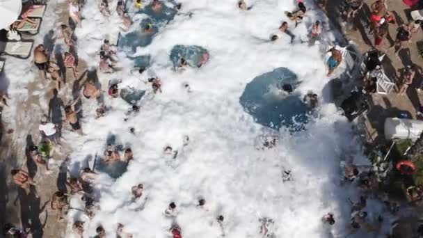 Crianças e adultos desfrutam de uma festa espumosa nadando na piscina em um dia quente de verão — Vídeo de Stock