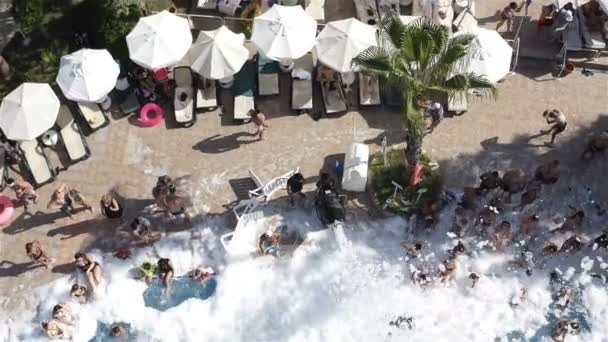 Espuma de sabão branco voa para fora do gerador, enchendo a piscina com turistas com cereais brancos — Vídeo de Stock