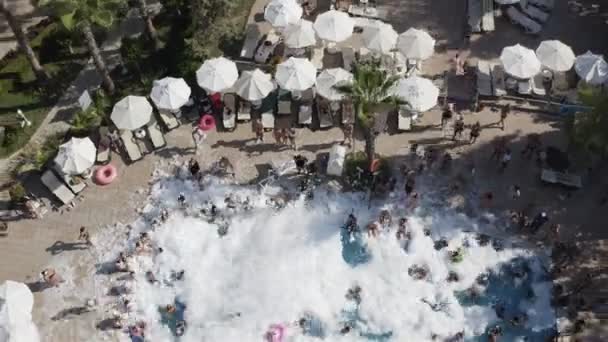 Bezzałogowy pojazd strzela do piankowej imprezy w basenie. Ludzie tańczą i kąpią się na otwartej przestrzeni. Szybsze strzelanie — Wideo stockowe