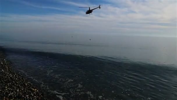 En helikopter flyger över sjökanten över turisternas huvuden — Stockvideo