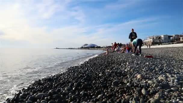 Turyści siedzą na kamiennej plaży o zachodzie słońca — Wideo stockowe