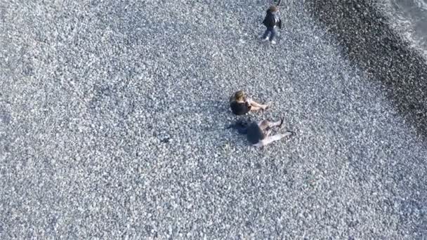 一对年轻夫妇坐在海边的一块大卵石上 — 图库视频影像