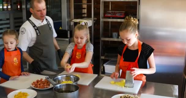 Повар помогает девочкам собирать тертый сыр — стоковое видео