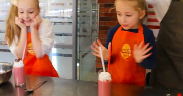 Köchin hilft Mädchen, Erdbeer-Smoothie mit Schlagsahne zu dekorieren