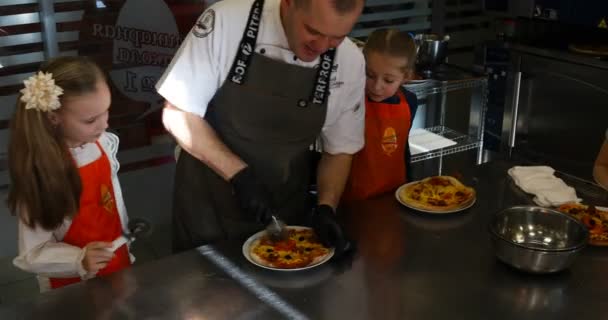 De chef helpt de meisjes pizza snijden — Stockvideo