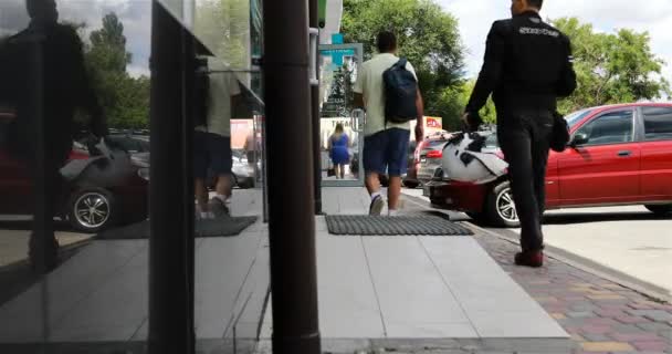 Egy fehér sisakos motoros elsétál egy bevásárlóközpont mellett. — Stock videók