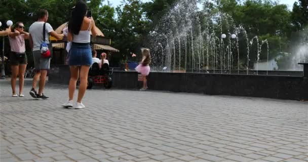 Девушка в розовой юбке счастливо прыгает рядом с фонтаном — стоковое видео