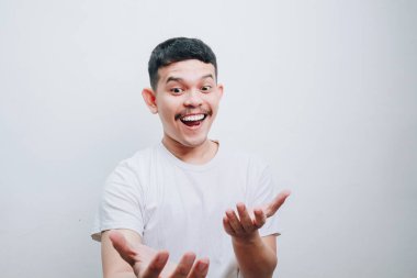Genç bir adam basit beyaz bir arkaplan karşısında avuçlarını açıp neşeli bir ifade sergiliyor. Görüntü mutluluk ve heyecan verir..