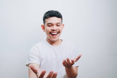 Genç bir adam geniş bir gülümseme ile ellerini uzatarak bir hoş geldin ya da ikram eder. Görüntü mutluluk ve cömertlik taşır..