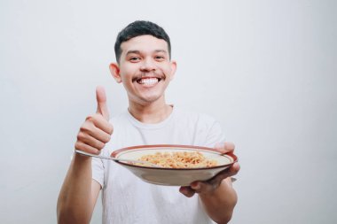 Gülümseyen bir adam elinde bir kase erişte tutarken başparmağını kaldırır. Mutlu ve tatmin edici ifade.