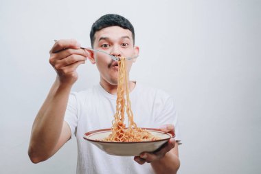 Genç bir adam bir kase erişteyi neşeyle elinde tutuyor ve yemek sevgisini gösteriyor..