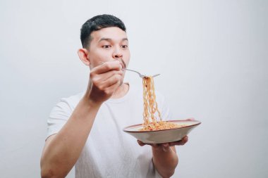 Şaşırmış genç bir adam lezzetli bir kase erişteden zevk alıyor, heyecan dolu..