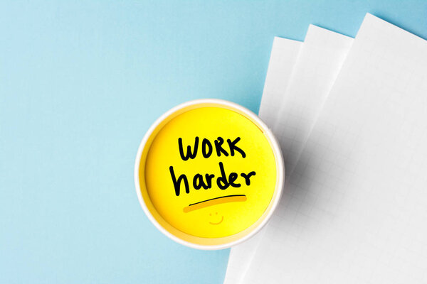 Work harder concept, handwriting message on cup with blue background and papers